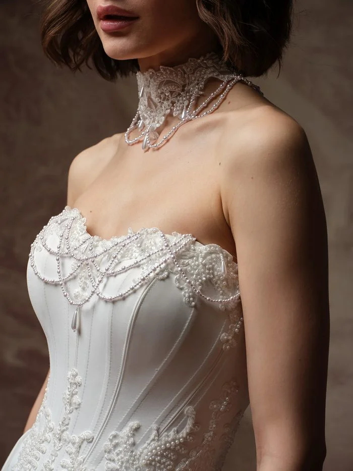 Close-up of the Seattle wedding dress choker by Maggie Sottero, a beaded lace collar with scalloped edges, swagged strands of small pearls, and teardrop pearl drops, worn above a strapless corset with matching pearl-draped lace at the neckline.