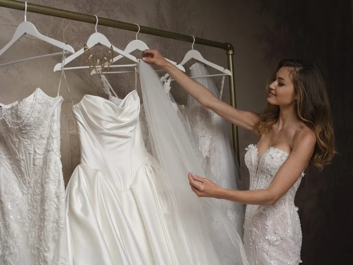 Bride browses a rack of wedding dresses at a bridal boutique, exploring different gown styles, fabrics, and silhouettes.