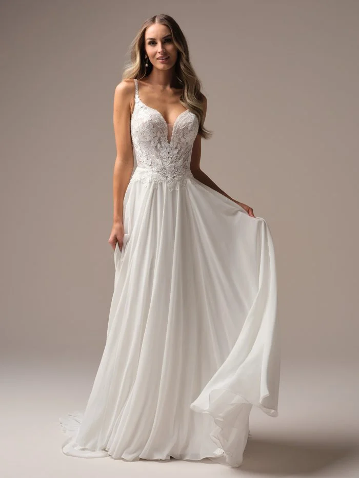 Full-length view of a bride in a flowing A-line wedding dress with a plunging lace bodice, delicate beaded straps, and a soft chiffon skirt.