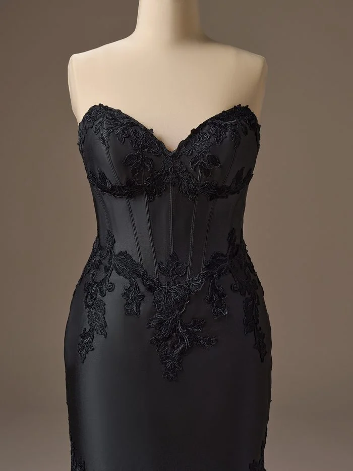Close-up detail of Serafina Lane by Maggie Sottero in Black, showcasing the structured corset bodice with a sweetheart neckline, visible boning, and tonal black floral lace appliqués cascading across the waist and bodice. The image highlights the gown’s architectural construction, rich satin fabric, and dimensional floral texture for a sophisticated monochromatic bridal look.