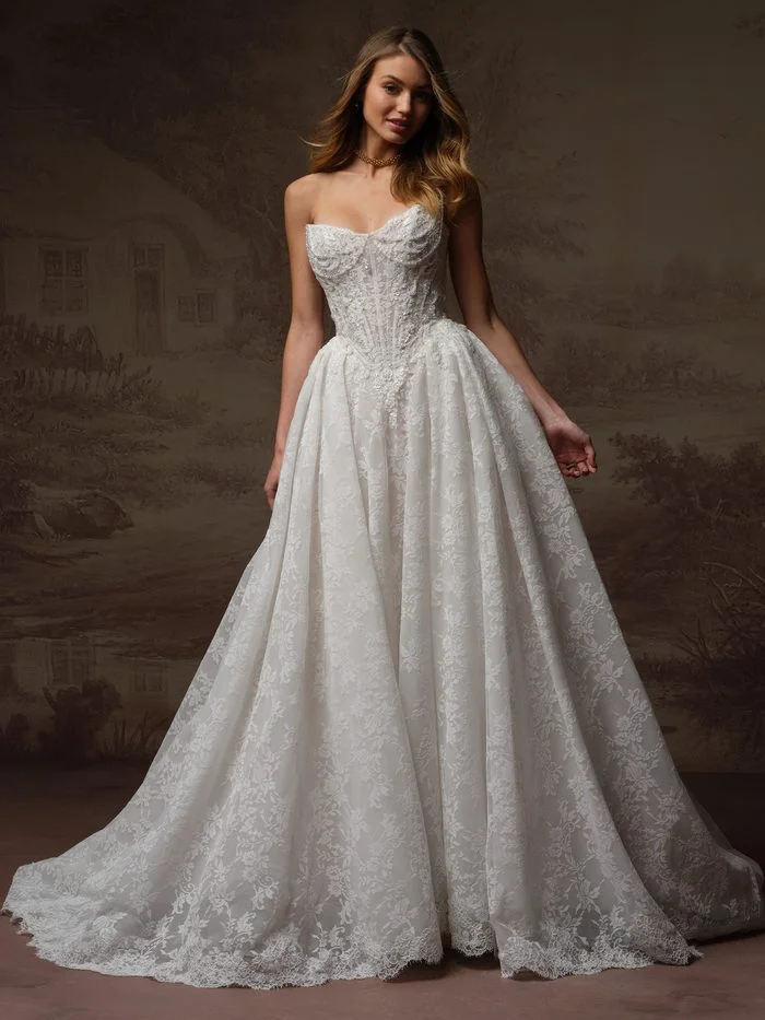Ryland by Maggie Sottero in Ivory over Blush, a ballgown wedding dress featuring a structured corset bodice with a sweetheart neckline, intricate lace appliqués, and pearl-accented beading throughout. The full skirt showcases an allover lace pattern with dramatic volume and a chapel-length train. Photographed in a studio setting, the gown highlights a romantic blend of classic ballgown styling and couture-inspired detailing.
