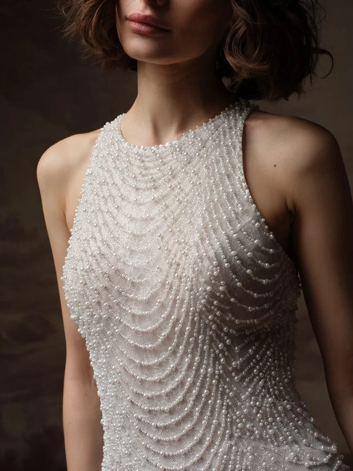 Close-up detail of Oleta by Sottero and Midgley in Ivory over Blush, showcasing intricate silver and pearl beading layered over delicate tulle. The image highlights the gown’s high illusion neckline, densely embellished bodice, and refined craftsmanship, with rows of pearls and metallic beading creating texture, shimmer, and an art deco-inspired design.