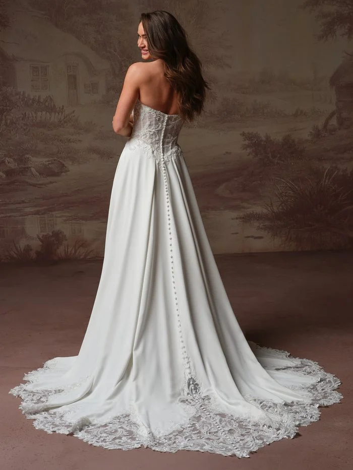 Back view of the Rebecca Ingram Hazel A-line wedding gown with covered buttons, lace detailing, and a sweeping lace-edged train.