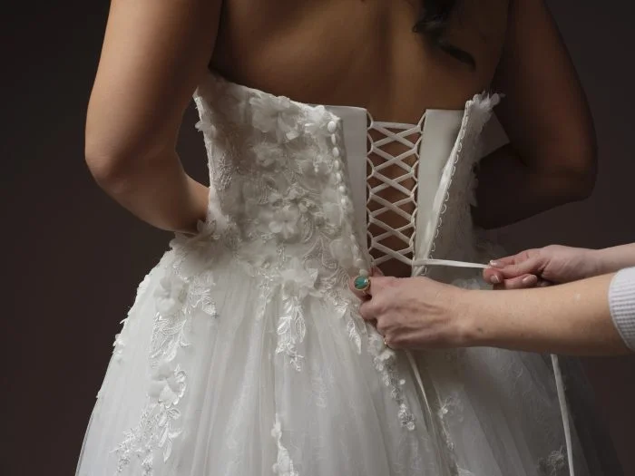 Close-up of a bride being laced into a floral lace wedding dress with a corset back and dimensional appliqués.