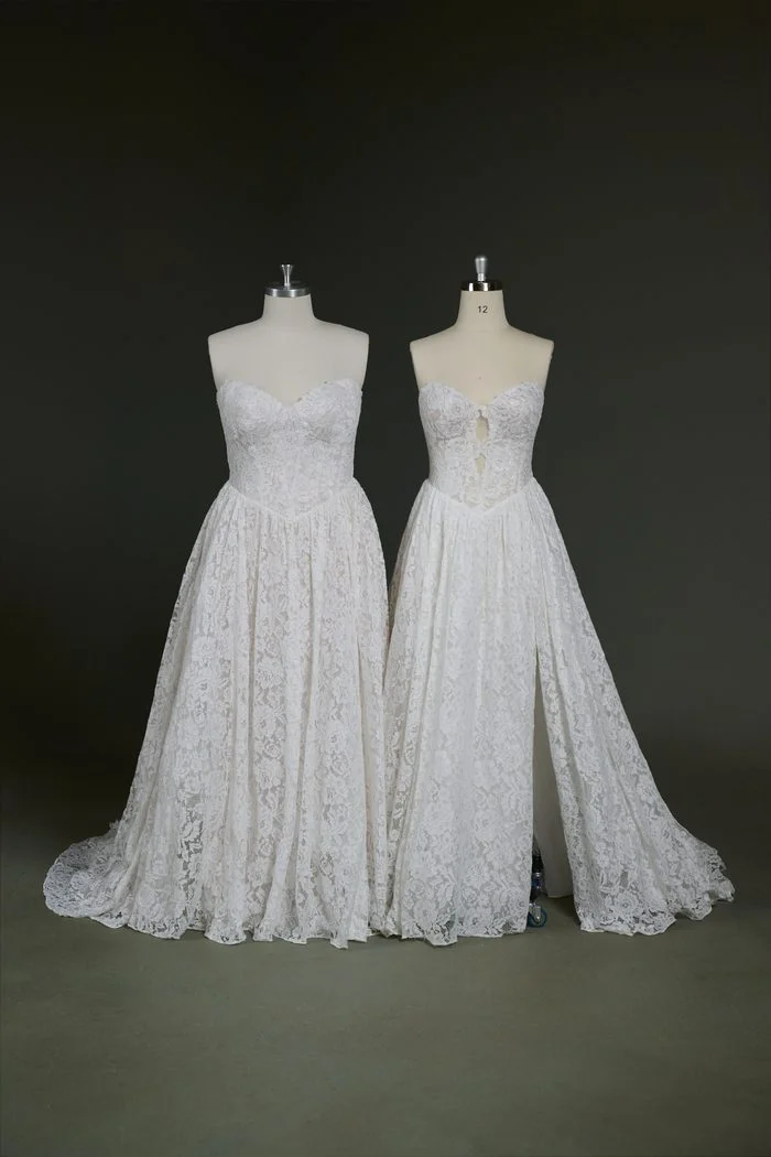 Two versions of the Narelle by Rebecca Ingram wedding gown are displayed side by side on dress forms. Both feature a strapless sweetheart neckline, allover floral lace, and an A-line silhouette. The gown on the left showcases a fully closed lace bodice and skirt, while the gown on the right features a front bodice keyhole cutout and a dramatic thigh-high slit, highlighting customizable design options.
