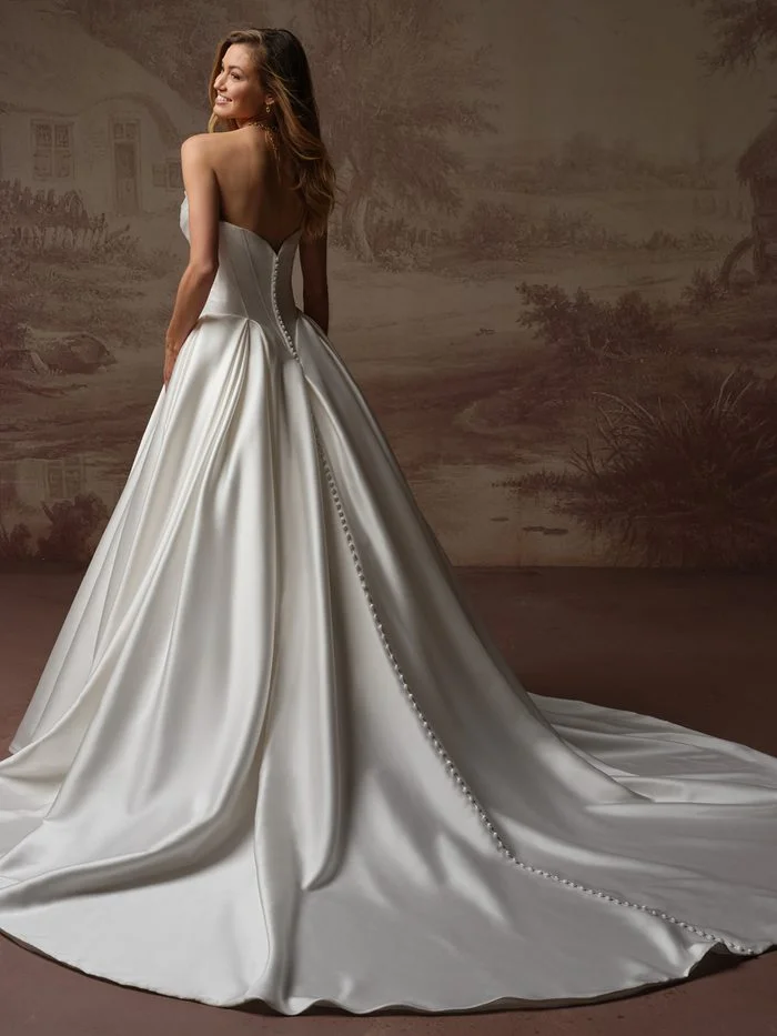 Back view of the Fiorita by Maggie Sottero wedding gown featuring a strapless satin ballgown silhouette with a fitted corset-inspired bodice and sweetheart back neckline. Covered buttons trail from the bodice down the center of the dramatic cathedral-length train, while box pleats at the waist create volume and structure throughout the full skirt.