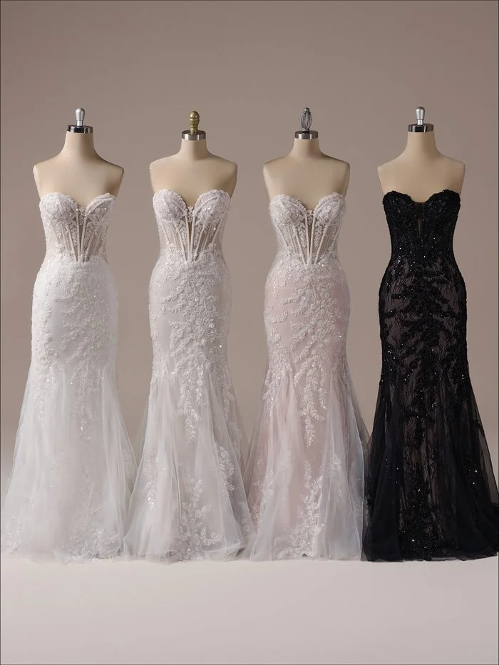 Four colorways of the Benjie Royale by Maggie Sottero wedding gown are displayed side by side on dress forms. Each gown features a fitted silhouette, a sheer corset bodice with exposed boning, intricate lace appliqués, and beaded embellishments. The lineup showcases different color combinations, including classic ivory, soft blush-toned variations, and a dramatic black colorway, highlighting the gown’s range of available color options.