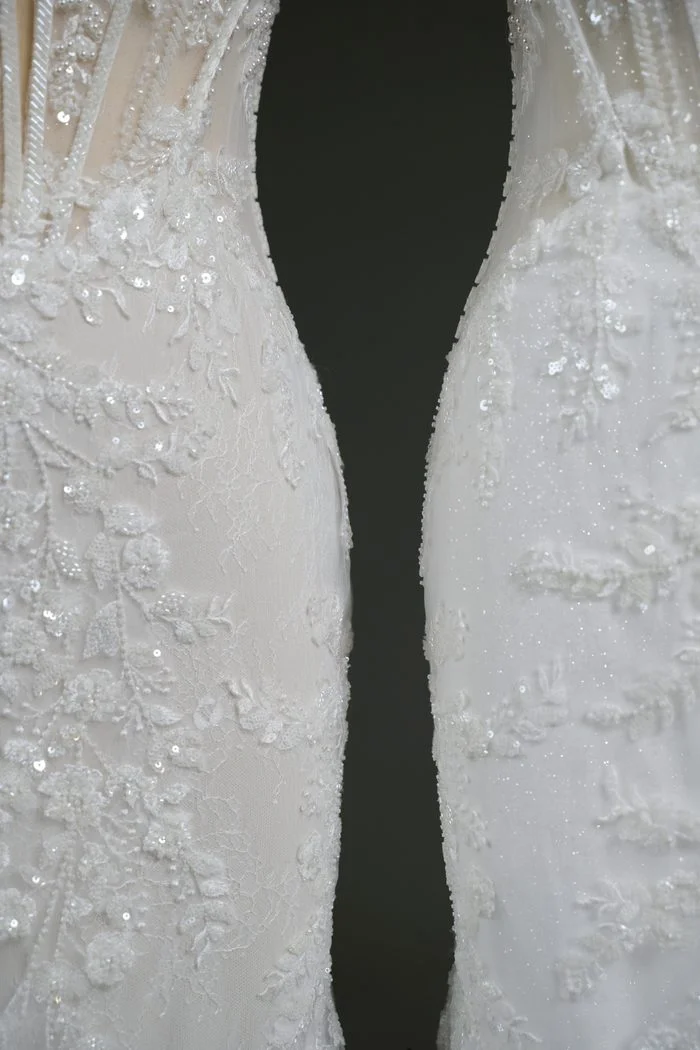 Close-up comparison of the skirt fabric on two Benjie Royale by Maggie Sottero wedding gowns. The gown on the left showcases lace appliqués layered over plain tulle, creating a soft, understated look. The gown on the right features the same lace appliqués over glitter tulle, with visible sparkle throughout the fabric, demonstrating a customizable skirt material option.
