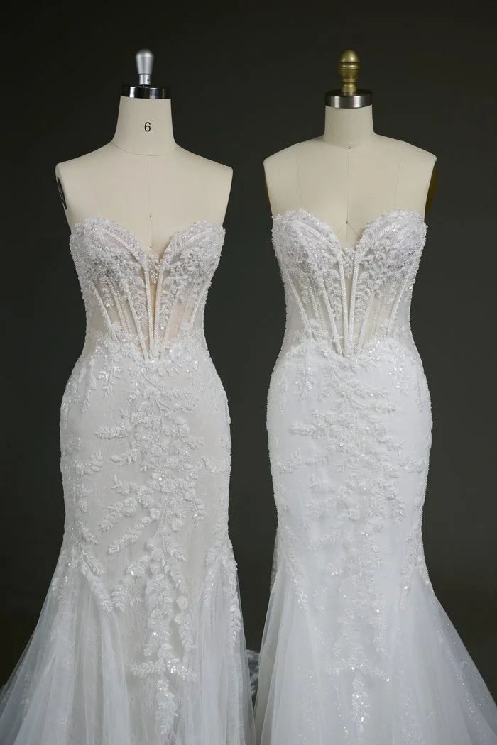 Two versions of the Benjie Royale by Maggie Sottero wedding gown are displayed side by side on dress forms. Both feature a fitted silhouette, a sheer corset bodice with exposed boning, and intricate lace appliqués with beaded embellishments. The gown on the left features a plain tulle skirt layer for a softer, matte finish, while the gown on the right incorporates glitter tulle beneath the lace, adding subtle shimmer throughout the skirt and train.