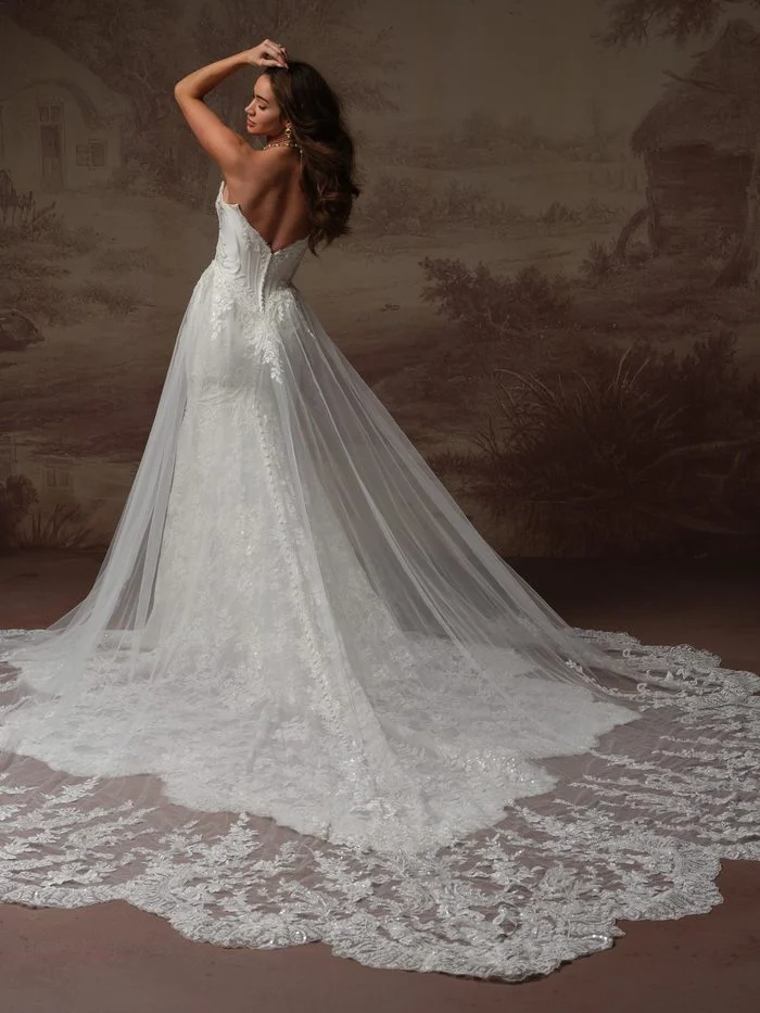 Back view of the Eirawen Bridal Train by Sottero and Midgley paired with a coordinating wedding gown. The detachable cathedral-length train is crafted from sheer tulle and adorned with intricate lace appliqués that extend into a dramatic scalloped lace border. Attached at the waist of a fitted lace gown with a low back and corset-inspired detailing, the train creates added volume, length, and romantic impact.