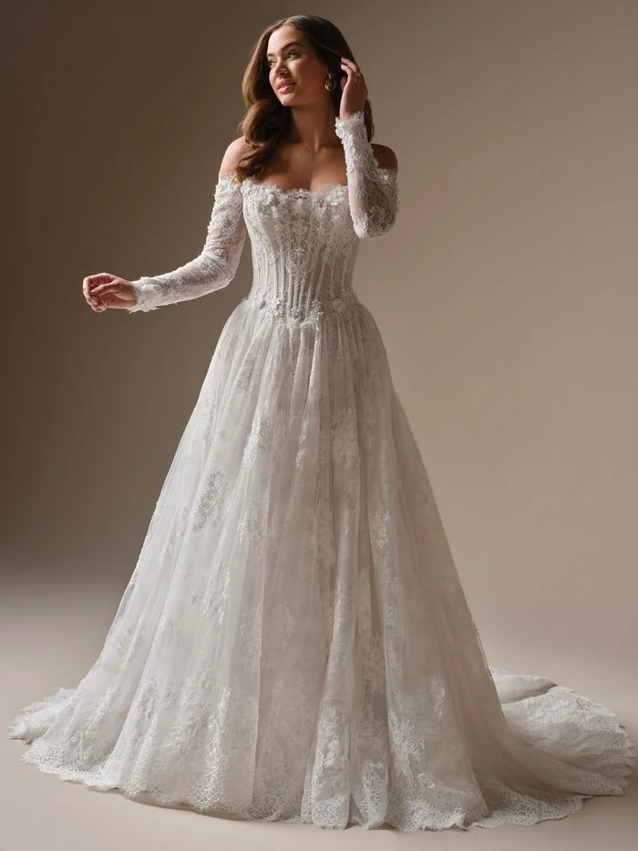 Maggie Sottero Kitaro ballgown wedding dress featuring an off-the-shoulder neckline, long lace sleeves, 3D floral lace, and a romantic basque waist.
