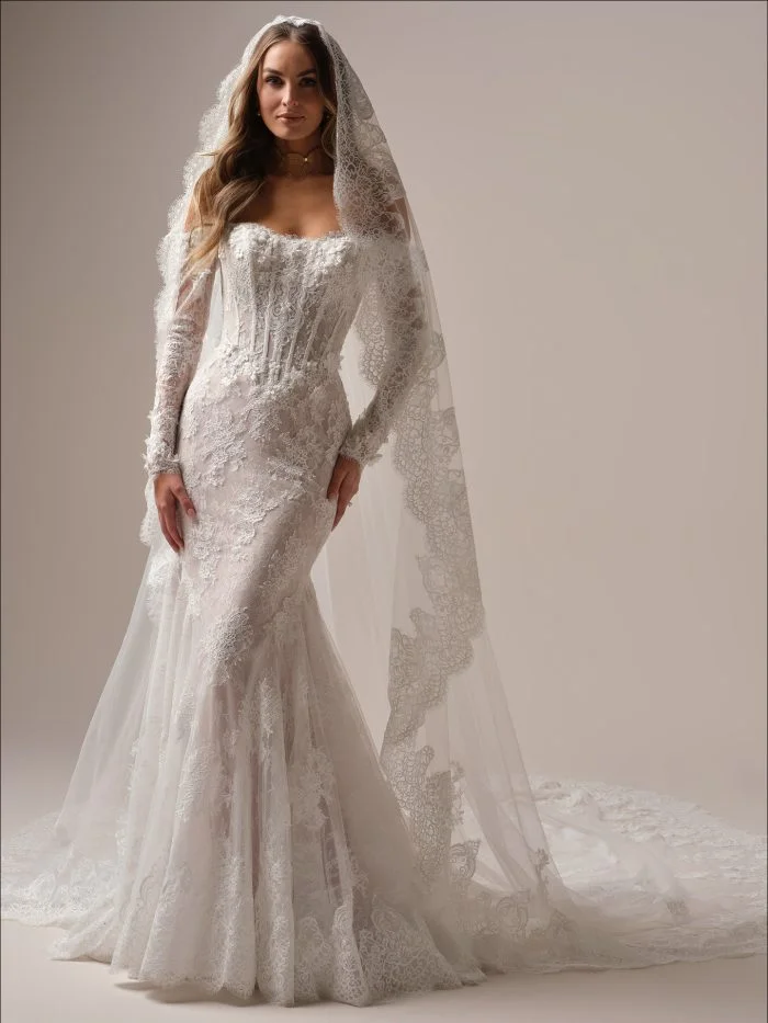 Maggie Sottero Takera mermaid wedding dress featuring an off-the-shoulder neckline, long lace sleeves, basque waist, and pearl-accented 3D floral lace.