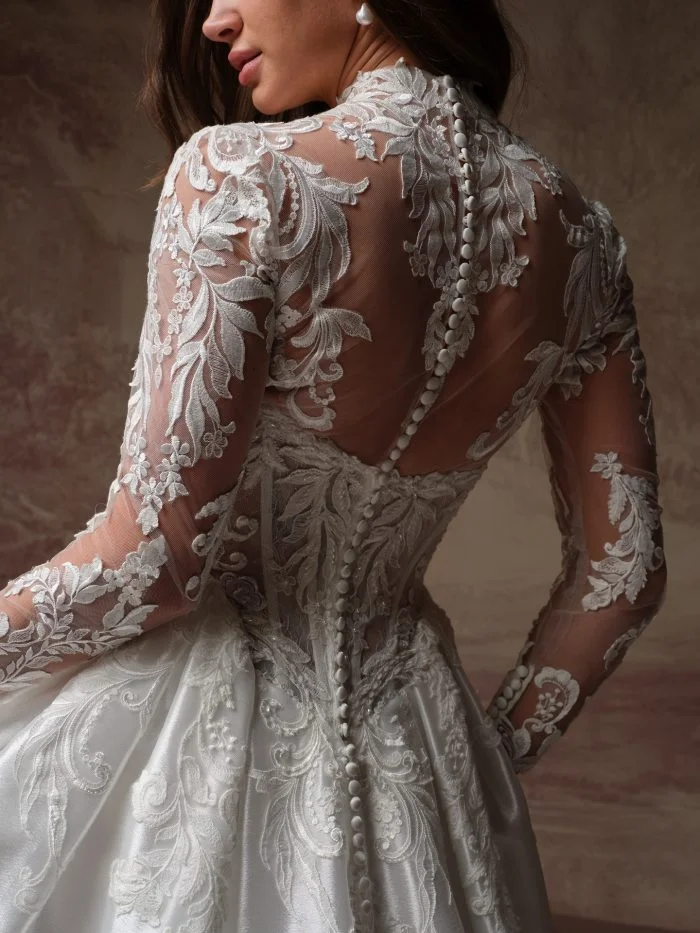 Maggie Sottero Dahlia ballgown wedding dress featuring a straight neckline, dramatic basque waist, embellished floral lace, and detachable long lace sleeves.