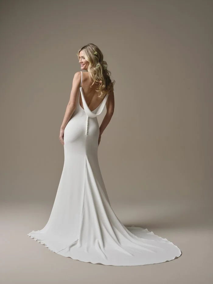 Back view of the Rebecca Ingram Brenda sheath wedding dress featuring a low draped back, delicate spaghetti straps, covered buttons, and a sleek train.