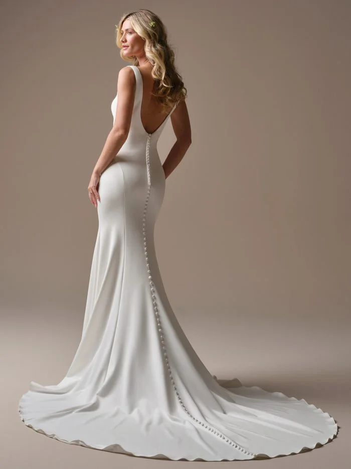 Back view of the Rebecca Ingram Lucille sheath wedding dress featuring a low draped back, delicate straps, and a sleek train.