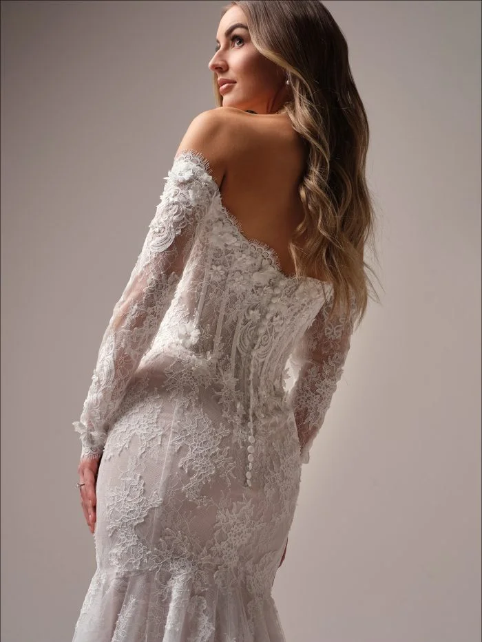 Close-up of the Takera fit-and-flare wedding dress by Maggie Sottero, highlighting the illusion lace back, fabric-covered buttons, and off-the-shoulder sleeves with floral detailing.