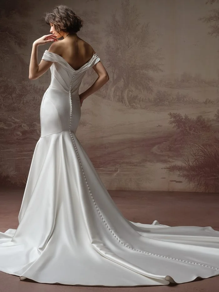 Back view of the Recine wedding dress featuring an off-the-shoulder neckline, button detail, and extended train.