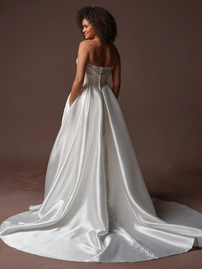 Back view of the Agatha wedding dress featuring a strapless bodice, button detail, and flowing satin train.