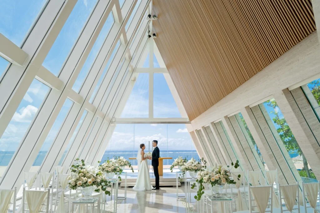 bride and groom at the altar inside an a-frame chapel with glass walls at Conrad Bali