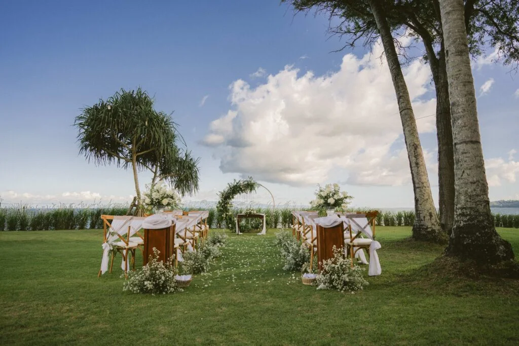 wedding setup with circular wedding arch decorated with white flowers on a garden by the beach - Aila Manggis