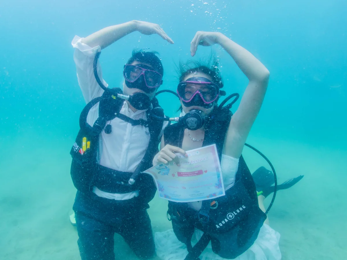 bride-and-groom-forming-a-heart-with-their-arms-while-holding-their-wedding-certificate-underwater-at-trang-thailand