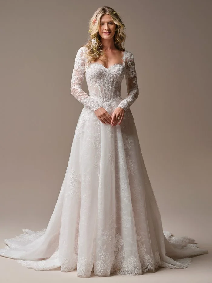 Esmeralda boho floral A-line wedding dress with sheer lace long sleeves, a sweetheart neckline, floral lace appliqués, and a flowing skirt with a romantic chapel train.