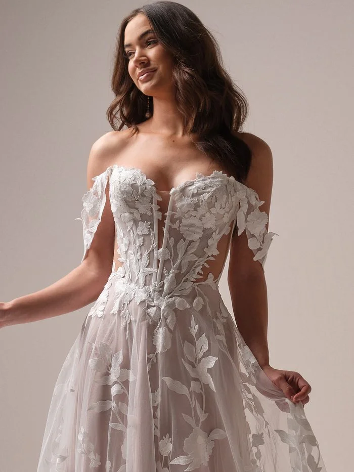 Natalie boho floral A-line wedding dress with detachable off-the-shoulder sleeves, featuring oversized floral appliqués, a sheer corset bodice, and dimensional botanical embroidery for a romantic bridal look.