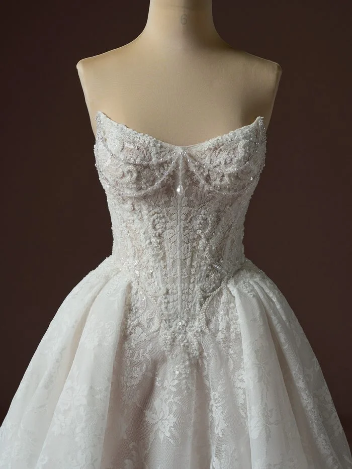 Close-up of the Ryland boho floral ballgown wedding dress featuring detachable beaded embellishments, a sparkling lace corset bodice, sweetheart neckline, and intricate floral lace detailing for a customizable bridal look.