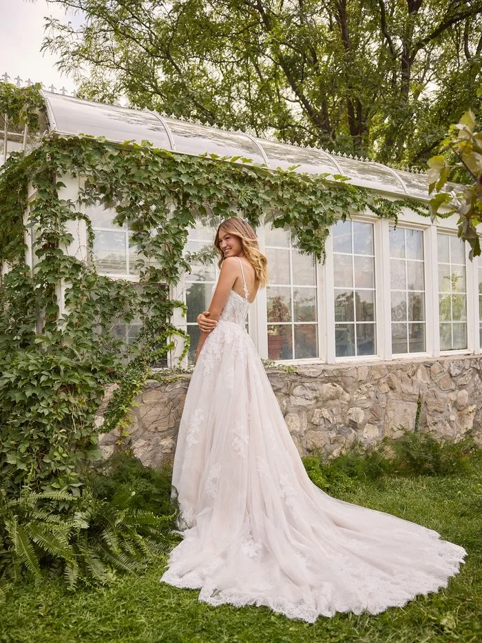 Back view of the Esmeralda boho floral A-line wedding dress featuring delicate lace straps, a soft tulle skirt, floral lace appliqués, and a sweeping train in a garden-inspired setting.