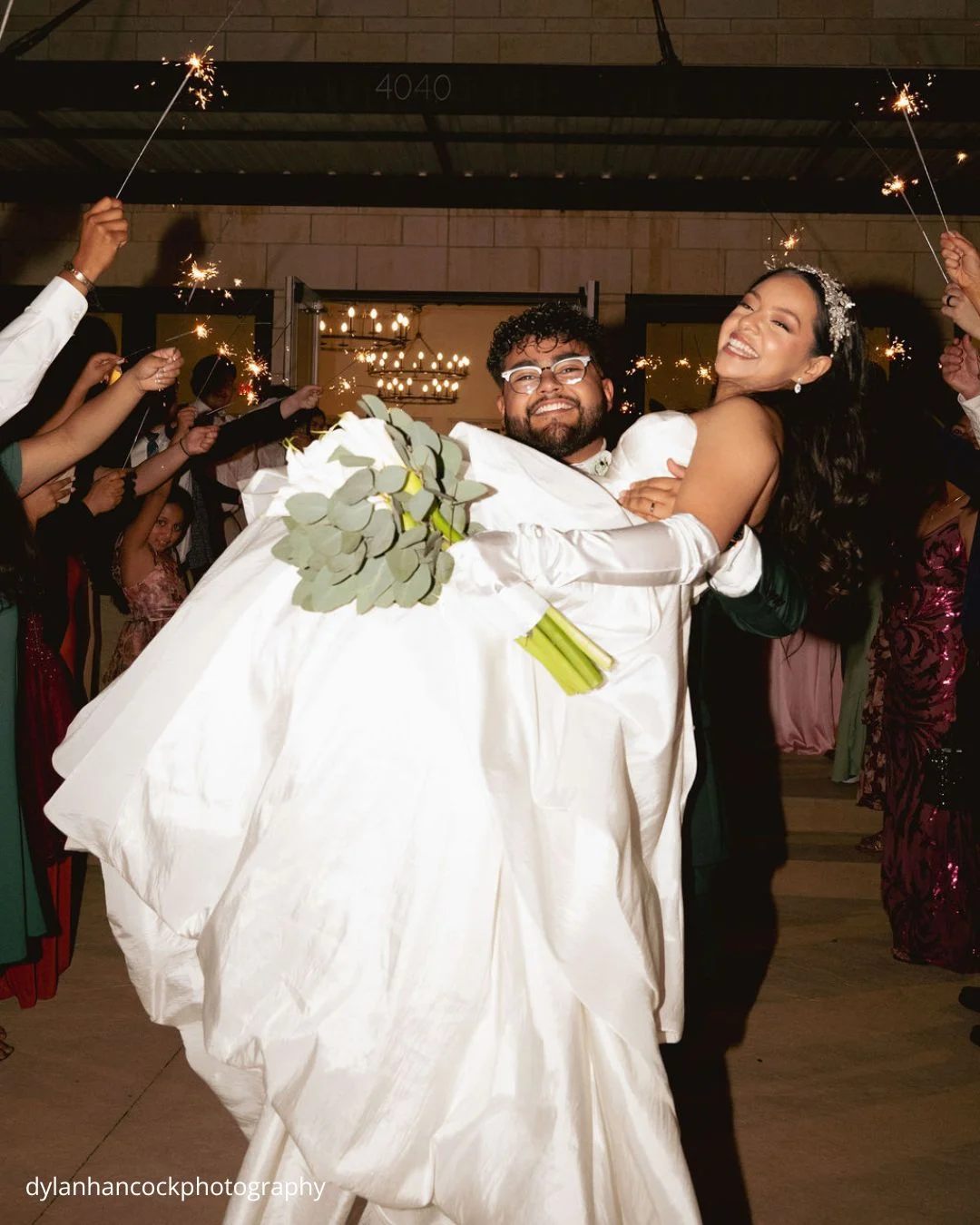 groom carries bride through guests holding sparklers dylanhancockphotography