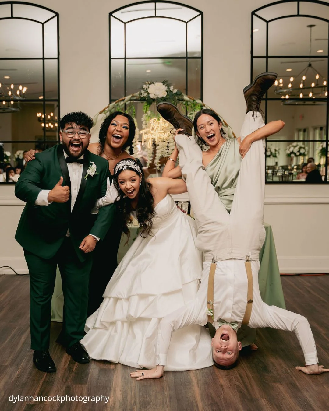 the bride groom and guests celebrate together with one guest playfully standing on their hands dylanhancockphotography