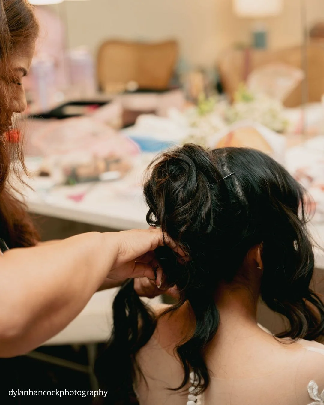 a bride in a white lace gown sits calmly as her mother carefully styles her hair before the wedding dylanhancockphotography