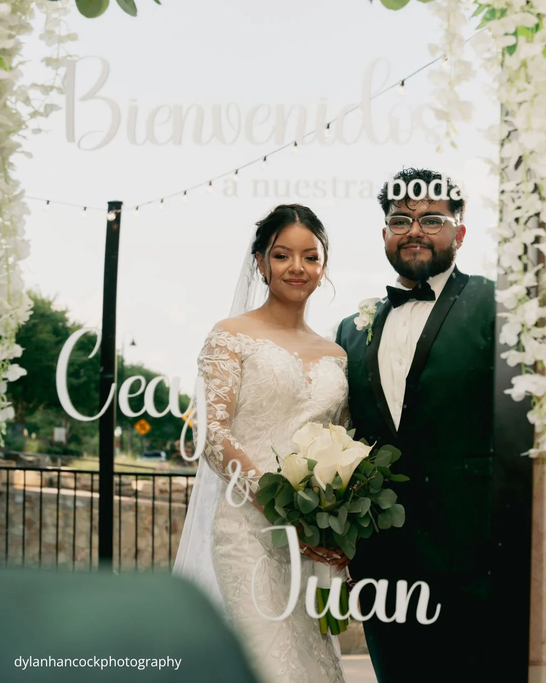 a couple dressed in their wedding attire stand smiling in front of a decorative mirror welcoming guests to their wedding dylanhancockphotography
