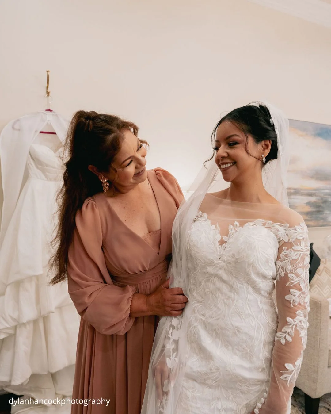 a bride in a white lace with a mom in a blush dress during wedding preparations dylanhancockphotography