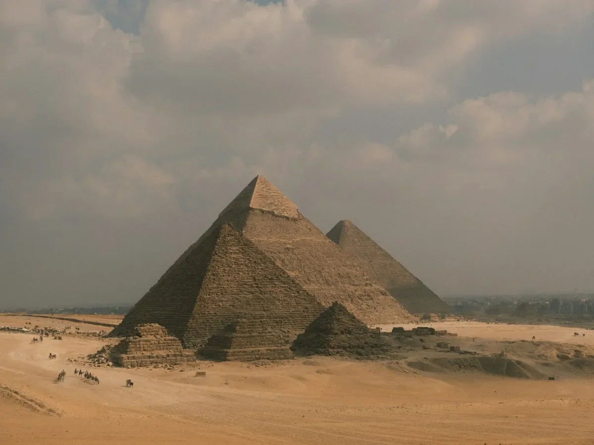 The Great Pyramids of Giza rising from the desert under a cloudy sky
