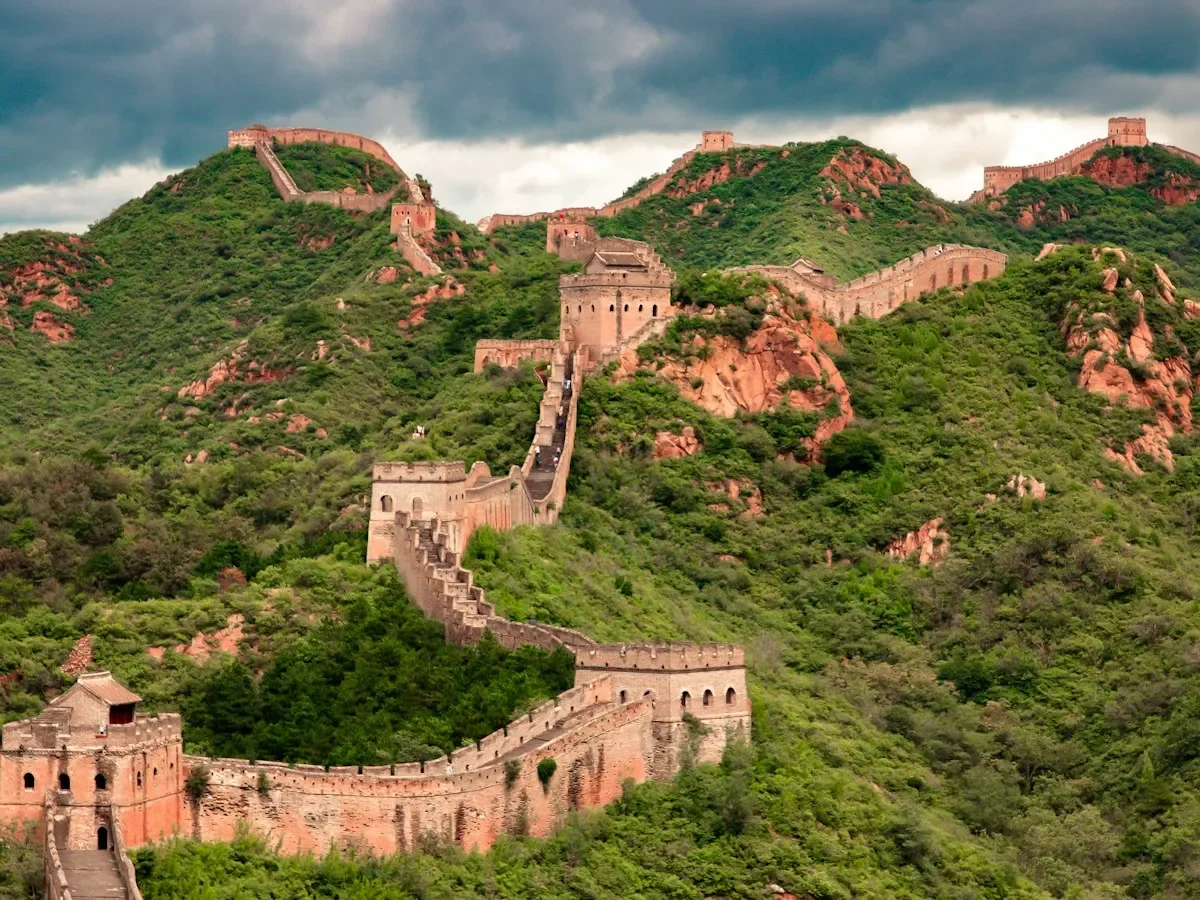 The Great Wall of China winding along green mountain ridges under a cloudy sky