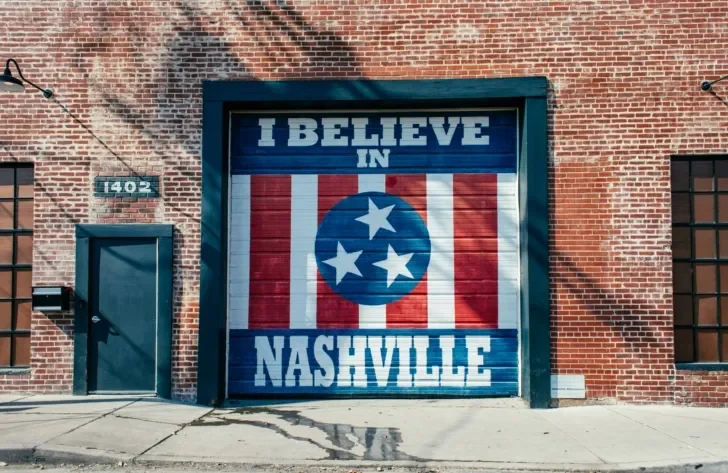 A vibrant mural on a red brick building features the iconic I Believe in Nashville design, incorporating the Tennessee flag’s three-star emblem against a red, white, and blue background.