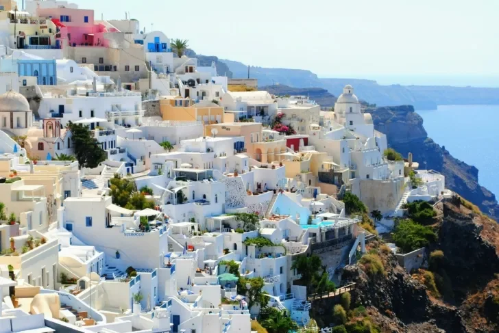 Scenic view of Santorini, Greece, showcasing white-washed buildings with blue domes cascading down a cliffside overlooking the Aegean Sea.
